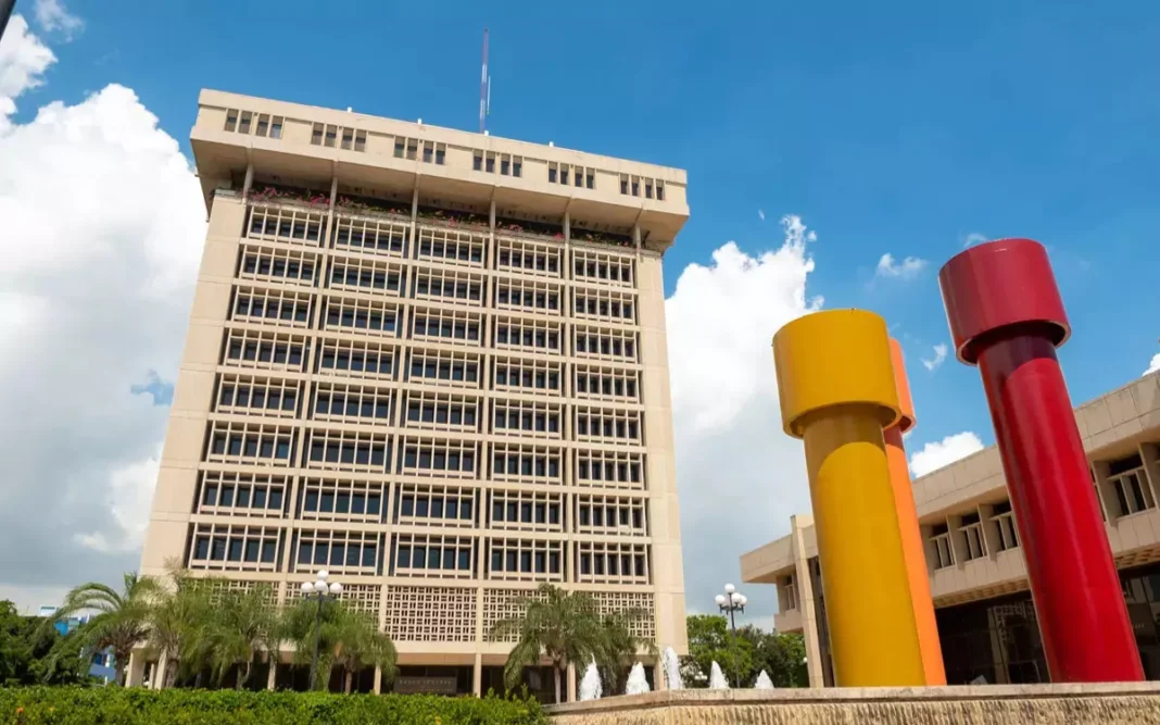 BCRD mantiene invariable su tasa de política monetaria El Banco Central de la República Dominicana (BCRD), en su reunión de política monetaria de enero de 2026, decidió mantener sin cambios su tasa de interés de política monetaria (TPM), en 5.25 % anual. Asimismo, la tasa de la facilidad permanente de expansión de liquidez (Repos a 1 día) permanece en 5.75 % anual, mientras la tasa de depósitos remunerados (Overnight) continúa en 4.50 % anual. Para esta medida se tomó en consideración el incremento de la incertidumbre global, así como las presiones inflacionarias recientes, asociadas principalmente al impacto de choques de oferta sobre los precios de los alimentos. Asimismo, se ponderó que el mecanismo de transmisión de la política monetaria ha estado operando de forma eficiente, lo que ha contribuido a condiciones financieras favorables a través de menores tasas de interés bancarias. En el entorno internacional, la economía de Estados Unidos de América (EUA) se ha mantenido resiliente con perspectivas de crecimiento que se revisan al alza hasta alcanzar 2.1 % en 2025 y 2.4 % en 2026, según el Fondo Monetario Internacional (FMI). En tanto, la inflación interanual se situó en 2.7 % en diciembre, por encima de la meta de 2.0 % de la Reserva Federal (Fed), mientras que se han moderado los riesgos de que continúe el debilitamiento del mercado laboral. Ante este panorama, la Fed mantuvo su tasa de interés de referencia en el rango de 3.50 – 3.75 % anual en su reunión de enero, previéndose que se reanuden los recortes de tasas de interés a mediados del presente año. En la Zona Euro, la actividad económica crecería 1.4 % en 2025 y 1.3 % en 2026, afectada por los conflictos geopolíticos y la incertidumbre comercial. Mientras, la inflación interanual se ubicó en 1.9 % en diciembre de 2025, en torno a la meta del Banco Central Europeo (BCE). En este contexto, los analistas de mercado esperan que el BCE mantenga su tasa de referencia sin cambios durante el año 2026. En América Latina, el crecimiento económico continuaría moderado, con una expansión prevista de 2.4 % en 2025 y 2.2 % en 2026, a la vez que la inflación permanece dentro del rango meta en casi todos los países. Luego de las reducciones en sus tasas de política monetaria durante el año 2025, la mayoría de los bancos centrales de la región mantuvieron sin cambios sus tasas de referencia en enero de 2026. Variación de TPM en 2025-2026 (puntos básicos) México -300 Uruguay -225 Guatemala -75 Costa Rica -75 Perú -75 RD -50 Chile -50 Colombia -25 Paraguay -25 Brasil +275 Respecto a las materias primas, el precio por barril del petróleo intermedio de Texas (WTI) incrementó recientemente hasta situarse en torno a US$65 al cierre de enero, influenciado por mayores tensiones geopolíticas. Asimismo, el precio del oro se sitúa en máximos históricos, por encima de los US$5,000 por onza troy, al ser utilizado como refugio de valor en un contexto de alta incertidumbre. La evolución del precio de este metal representa una mejoría en los términos de intercambio para la República Dominicana, lo que continuaría influenciando positivamente la cuenta corriente de la balanza de pagos. En el entorno nacional, la inflación interanual se ubicó en 4.95 % en diciembre de 2025, dentro del rango meta de 4.0 % ± 1.0 %. No obstante, los precios de los alimentos continúan afectados por choques de oferta exógenos a la política monetaria, tales como el impacto de eventos climáticos, que incidieron en la producción y comercialización de bienes agropecuarios. Asimismo, la inflación subyacente ha sido afectada por los incrementos en los servicios de suministro de alimentos ante los mayores precios de estos insumos, ubicándose en 4.85 % interanual, dentro del rango meta establecido en el programa monetario. El sistema de pronósticos del BCRD señala que, si bien la inflación local continuaría afectada en el corto plazo por estos choques, se prevé que su impacto se disiparía gradualmente durante los próximos trimestres en la medida que se normalicen las condiciones de oferta. De esta forma, se espera que la inflación general y la subyacente se ubiquen dentro del rango meta de 4.0 % ± 1.0 % al cierre del año 2026. Asimismo, los analistas del mercado esperan que las presiones inflacionarias recientes se moderen durante el presente año, manteniendo ancladas sus expectativas de mediano plazo en torno a 4 %, centro del rango meta. Por otro lado, el indicador mensual de actividad económica (IMAE) registró una expansión interanual de 2.3 % en el mes de diciembre. De esta forma el crecimiento acumulado en el año 2025 se ubicó en 2.1 %, impulsado principalmente por los sectores de agropecuaria y minería; así como por los servicios de intermediación financiera y hoteles, bares y restaurantes, entre otros. Hacia adelante se prevé una recuperación gradual de la actividad económica, con una expansión proyectada en torno a 4.0 % para el año 2026, apoyada en un mayor ritmo de ejecución de la inversión pública y en condiciones financieras favorables. Es importante destacar que, el BCRD redujo la TPM en 50 puntos básicos de forma acumulada en el segundo semestre de 2025, ubicándola en torno a una postura monetaria neutral, al considerar las expectativas de inflación. A la vez, el BCRD implementó el programa de provisión de liquidez de RD$81 mil millones aprobado por la Junta Monetaria para la canalización de financiamiento a los sectores productivos en condiciones favorables. En la medida que ha estado operando el mecanismo de transmisión de la política monetaria, las condiciones financieras se han flexibilizado, lo que contribuiría a dinamizar la demanda interna. En efecto, se ha observado una disminución significativa en la tasa de interés interbancaria al pasar de un máximo de 12.6 % en junio de 2025 a 7.1 % anual en enero de 2026. Asimismo, la tasa pasiva promedio ponderado de la banca múltiple ha disminuido de 9.6 % a 5.9 % con respecto a enero de 2025; mientras que la tasa activa promedio ponderado ha bajado de 15.2 % a 13.5 % en el mismo periodo. En tanto, el crédito al sector privado en moneda nacional ha registrado un crecimiento interanual en torno a 8 % en enero, impulsado por los préstamos a los sectores productivos. Asimismo, los agregados monetarios se expanden a tasas superiores al crecimiento del PIB nominal. En cuanto al sector externo, las remesas alcanzaron US$11,866.3 millones al cierre de 2025 (crecimiento de 10.3 %), mientras las exportaciones totales ascendieron a US$ 15,930.6 millones (14.4 %) impulsadas por las mayores exportaciones de oro. En ese sentido, se estima que el déficit de cuenta corriente se ubicaría en torno a 2.4 % del PIB en 2025, siendo totalmente financiado por la inversión extranjera directa proyectada de US$4,900 millones. El buen desempeño de las actividades generadoras de divisas ha contribuido al mantenimiento de la estabilidad relativa del tipo de cambio, con una depreciación interanual de 3.1 % en 2025 y de alrededor de 2.0 % en el mes de enero. Asimismo, las reservas internacionales se ubicaron al cierre del año 2025 en unos US$14,700 millones, equivalente a más de 11 % del PIB y 5 meses de importaciones, superando las métricas recomendadas por el FMI. Es importante resaltar que la economía dominicana cuenta con fuertes fundamentos y un sector productivo resiliente, que se reflejan en una mejor percepción de riesgo país con relación al promedio de América Latina y otras economías emergentes. En este entorno internacional desafiante, el Banco Central de la República Dominicana seguirá monitoreando la evolución de la economía y evaluando los espacios para continuar adoptando oportunamente las medidas que contribuyan a impulsar la actividad económica, reiterando su compromiso de mantener la inflación dentro del rango meta. 29 de enero de 2026